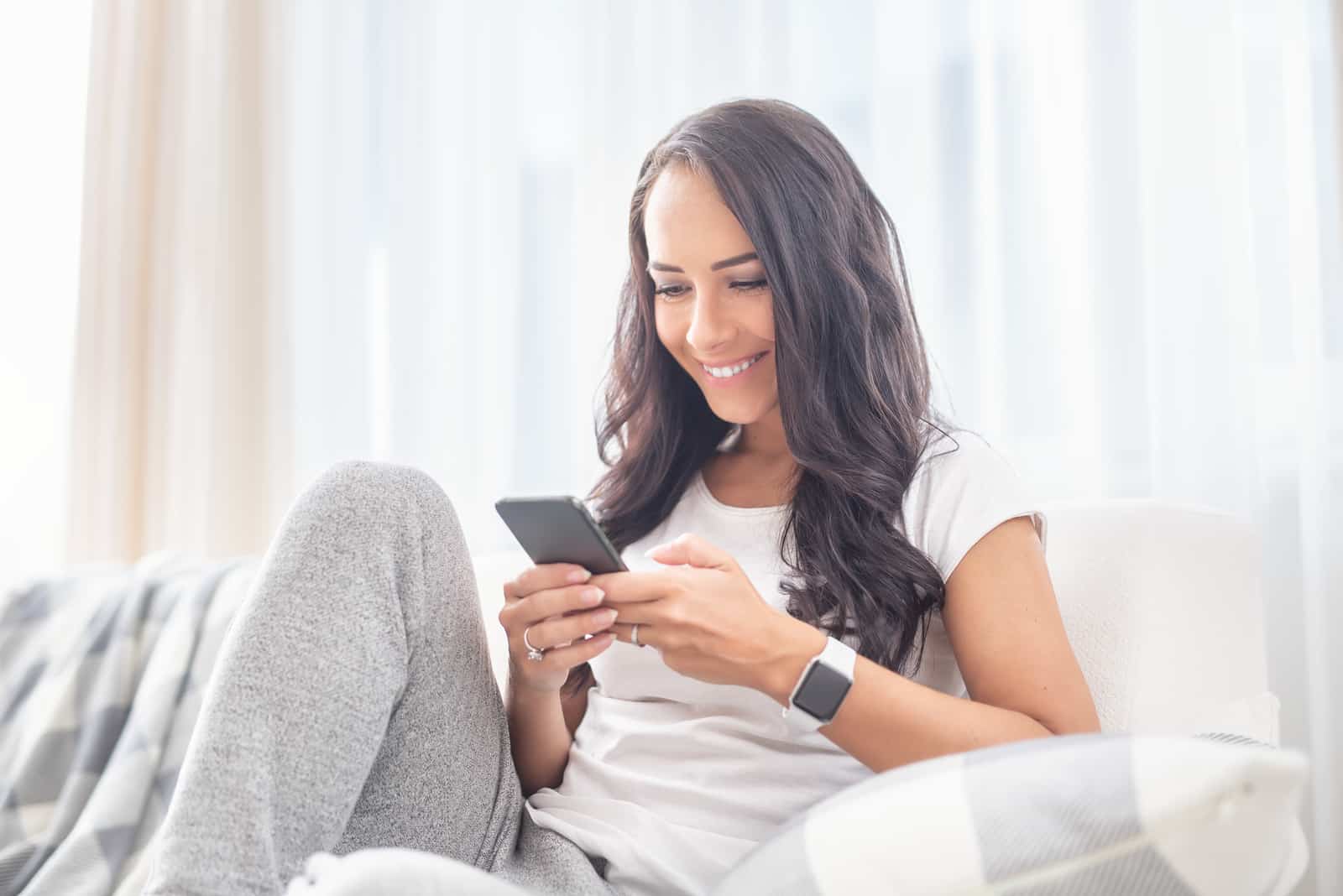 Une femme aux longs cheveux bruns est assise sur le canapé et appuie sur un bouton du téléphone