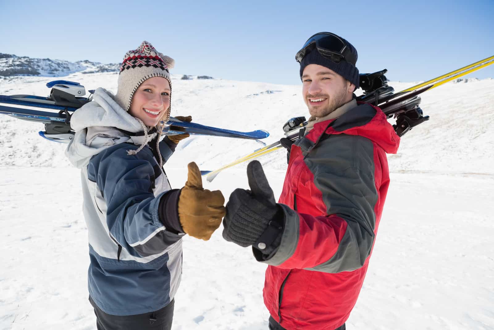 Vue arrière portrait d'un couple souriant avec des planches de ski faisant des gestes sur le paysage couvert de neige
