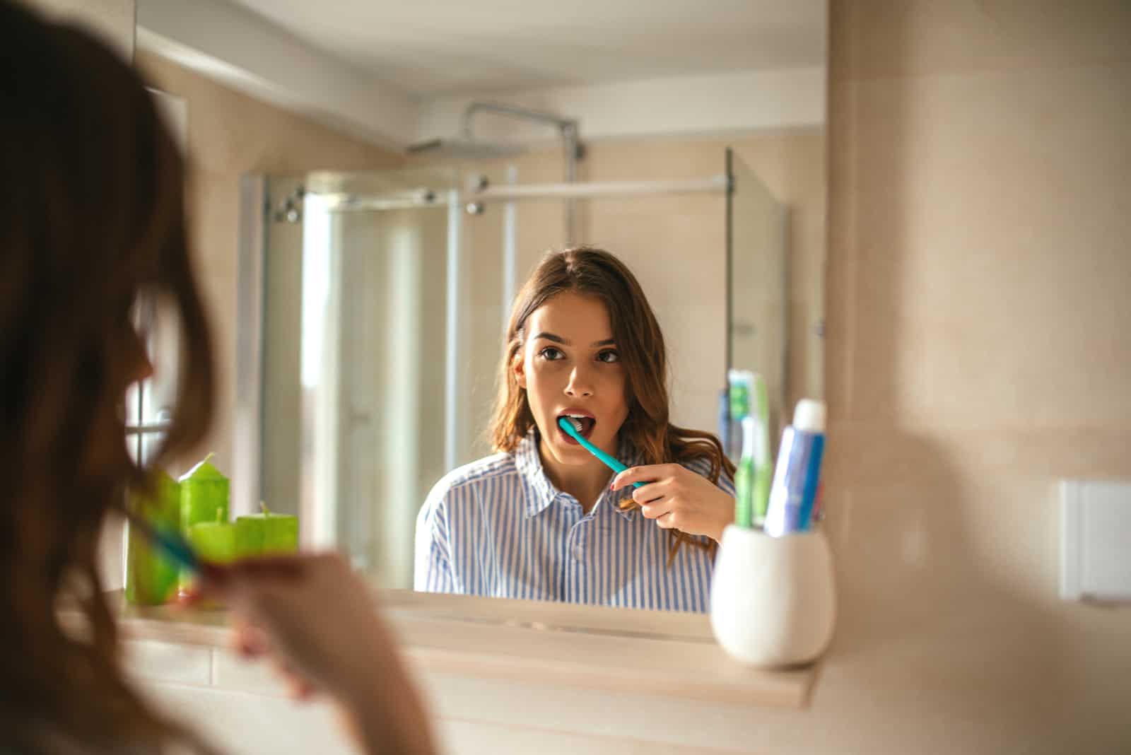 belle femme se brosser les dents et regarder dans le miroir