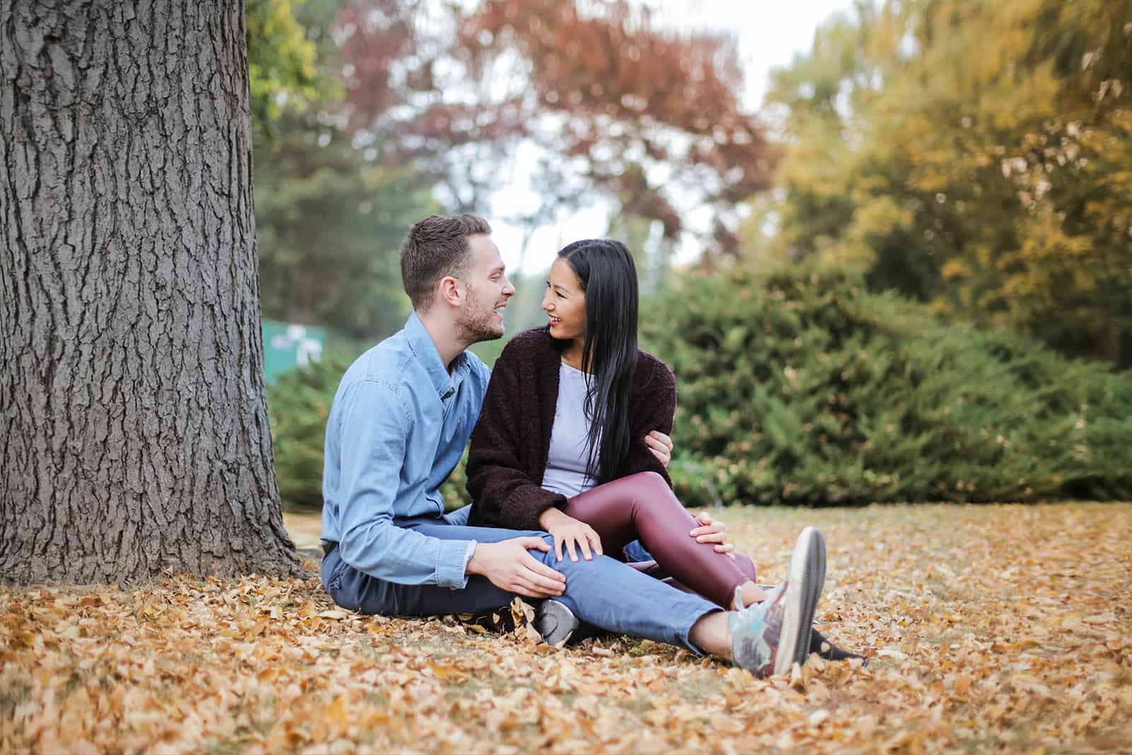 un couple parlant sous un arbre et assis sur des feuilles sèches