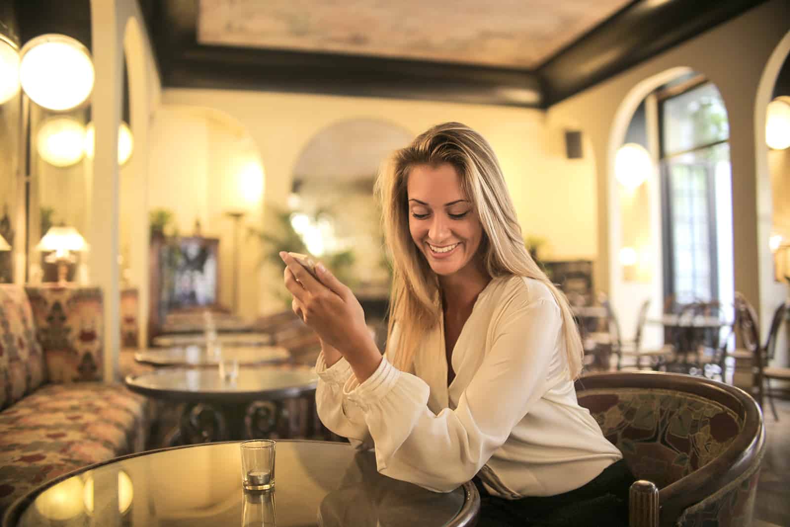femme joyeuse lisant un message du téléphone alors qu'il était assis dans le bar