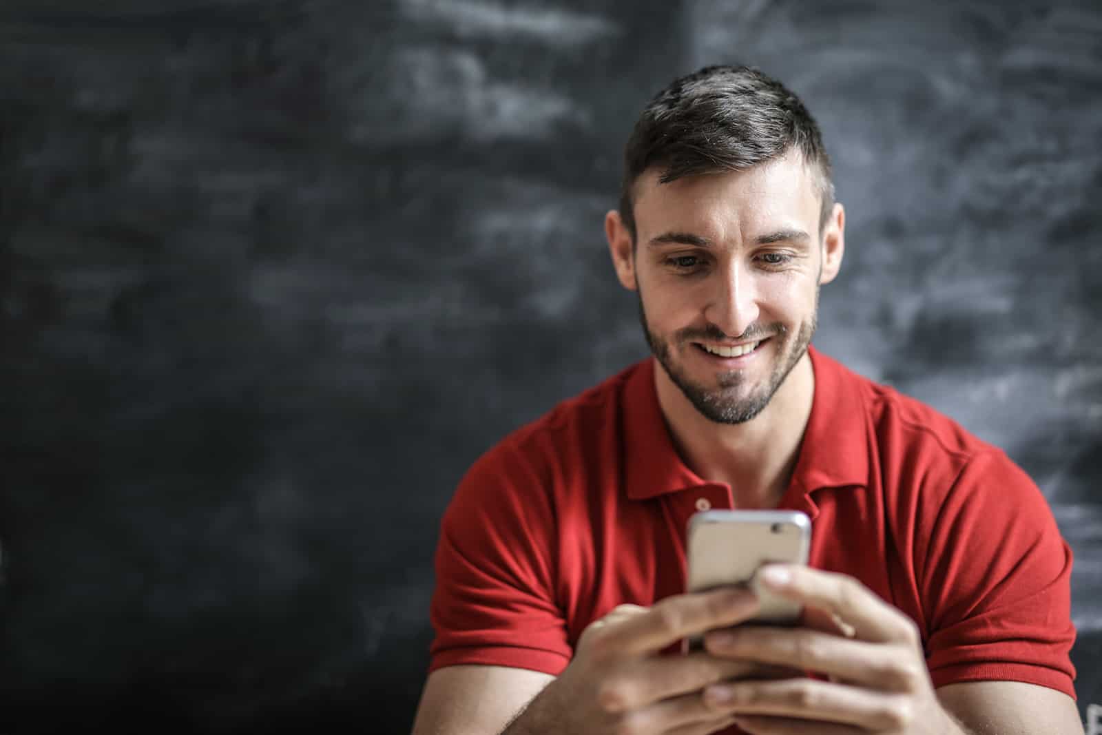 un homme en t-shirt rouge tapant sur un smartphone et souriant