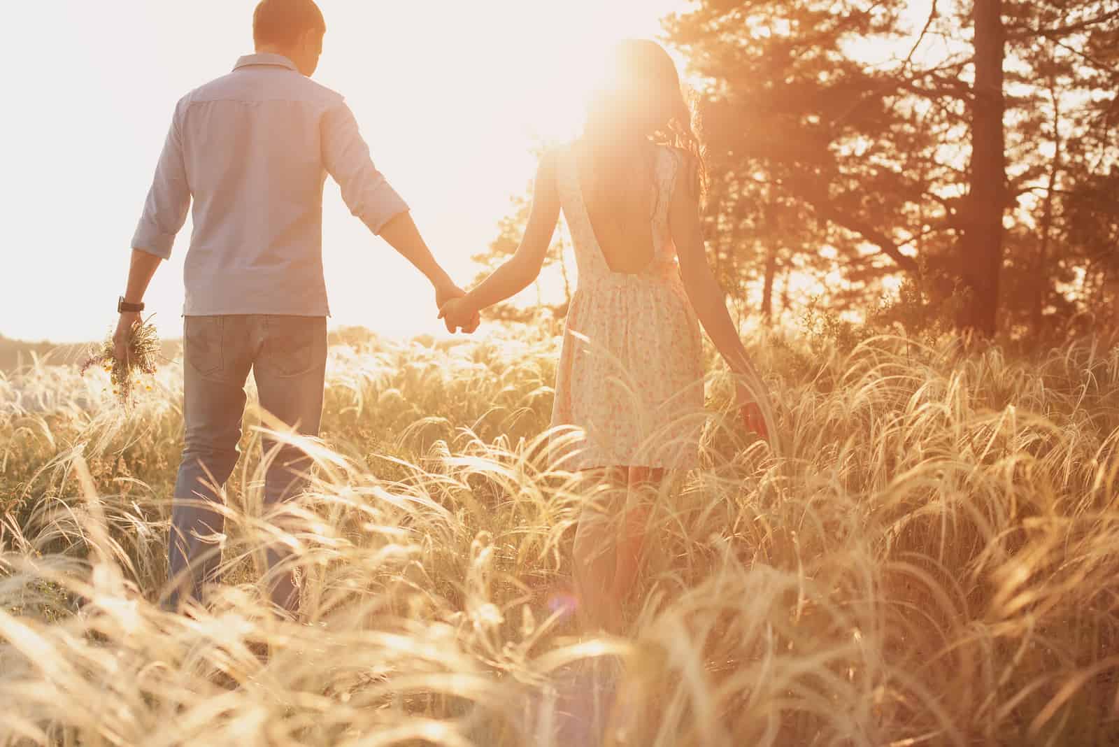 un homme et une femme marchent dans le champ en se tenant la main