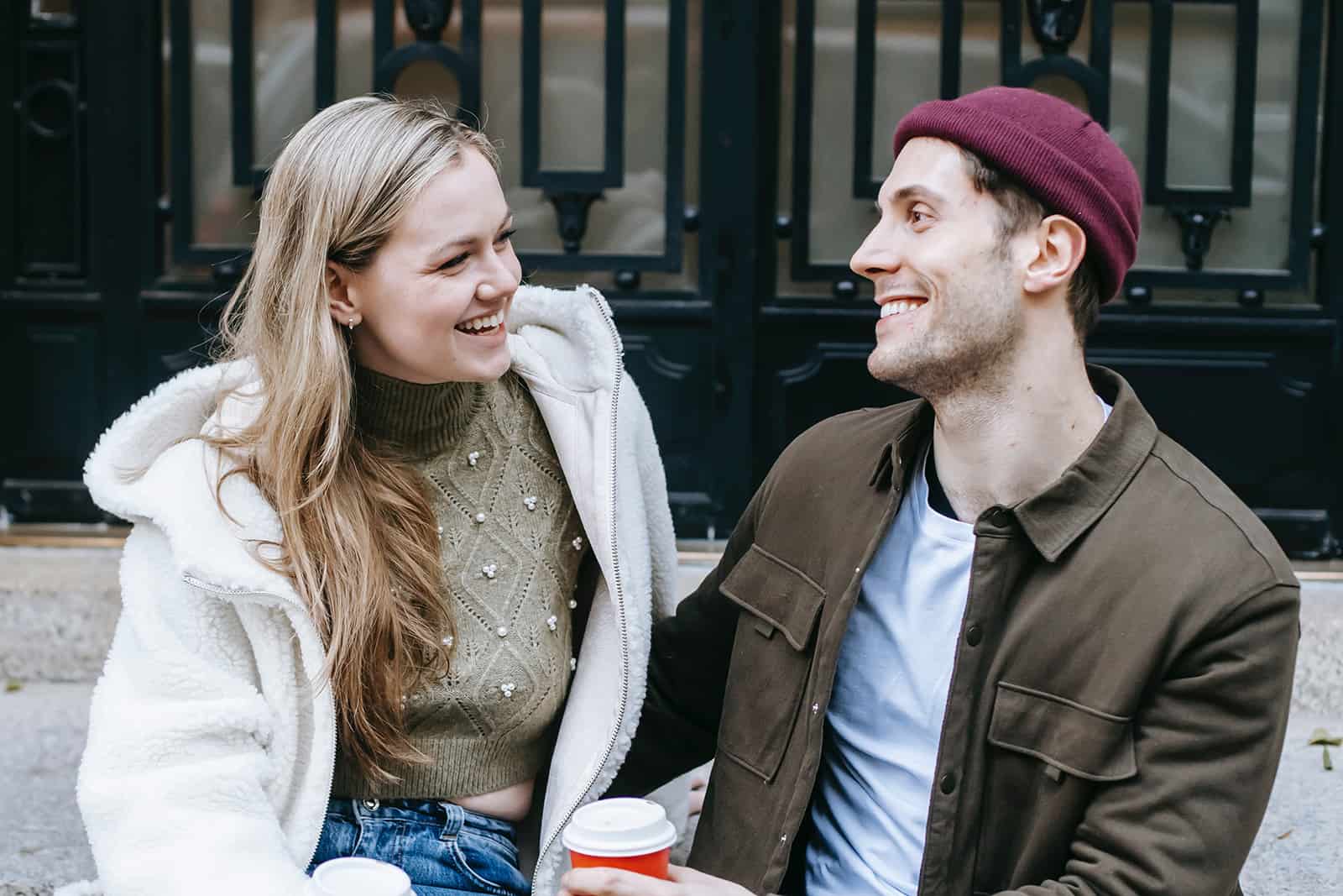 un homme et une femme riant et buvant du café devant le bâtiment