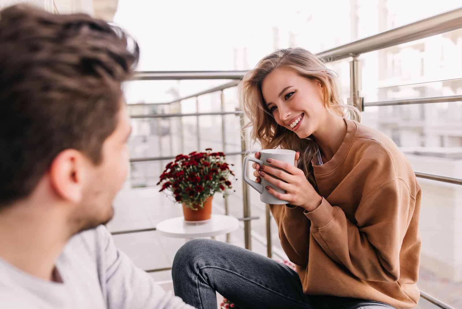 un homme et une femme sont assis en train de boire du café sur le balcon et de rire