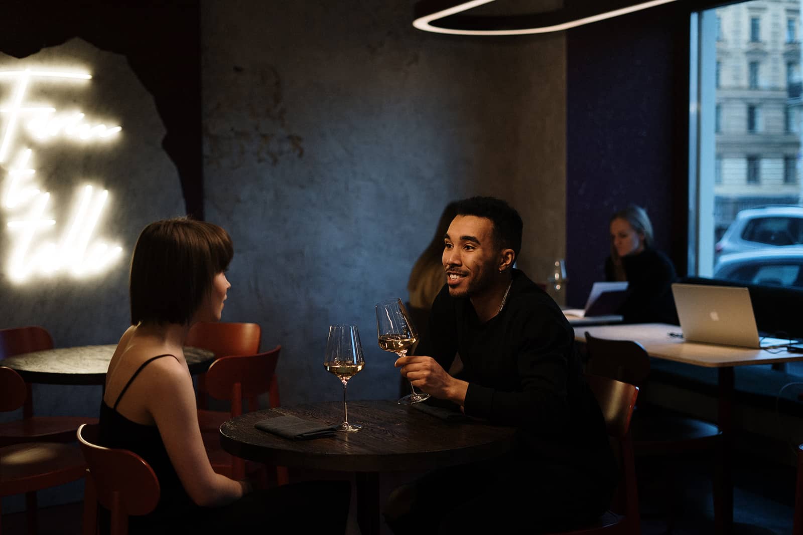 Un homme souriant regardant une femme assise dans un restaurant avec lui et buvant du vin ensemble