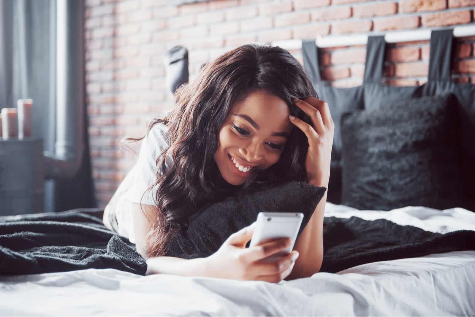 une belle femme aux longs cheveux noirs se trouve sur le lit tout en tenant le téléphone dans sa main