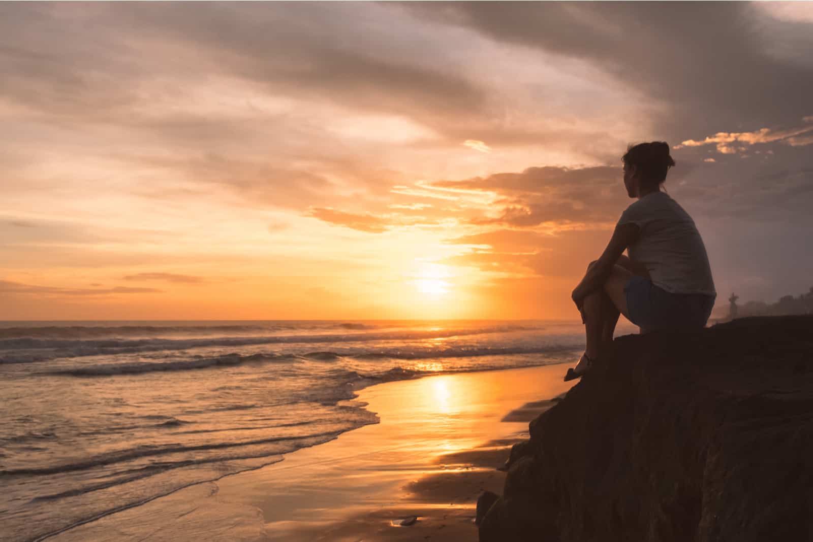 une femme imaginaire est assise sur un rocher et regarde la mer