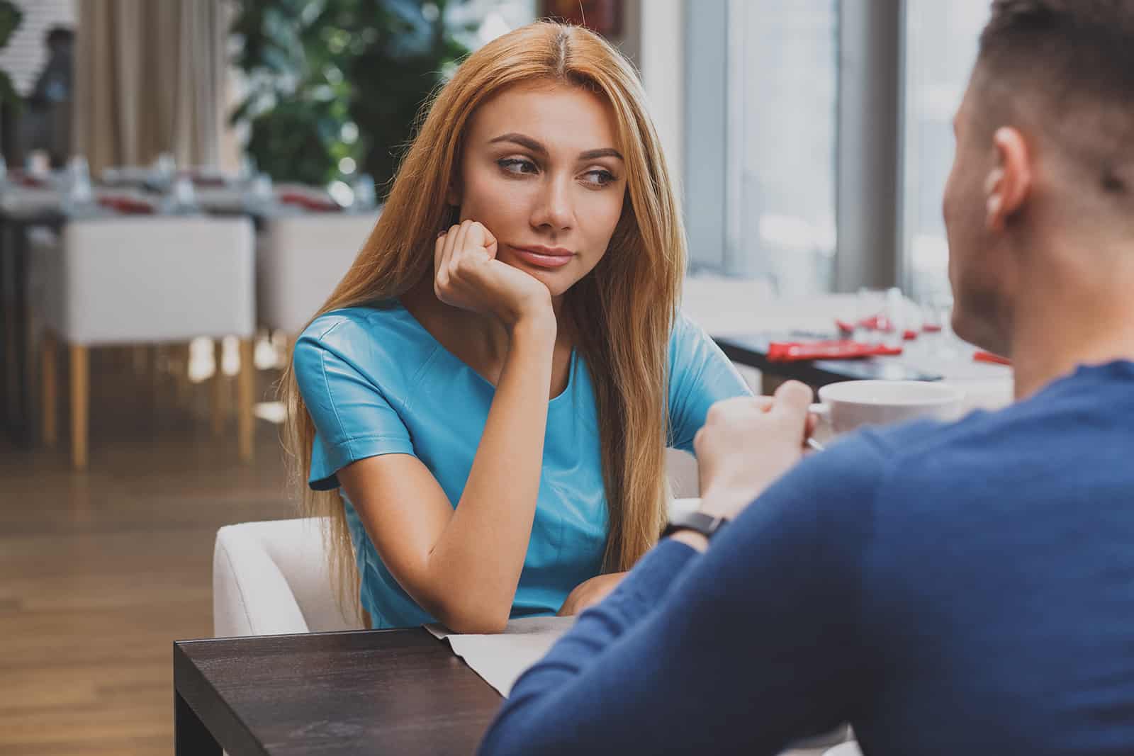 Une femme pensive regardant de côté alors qu'il était assis avec un homme dans un café à une date