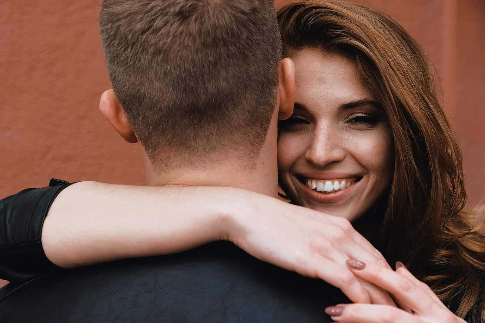 Une femme souriante étreignant son petit ami tout en se tenant près du mur ensemble