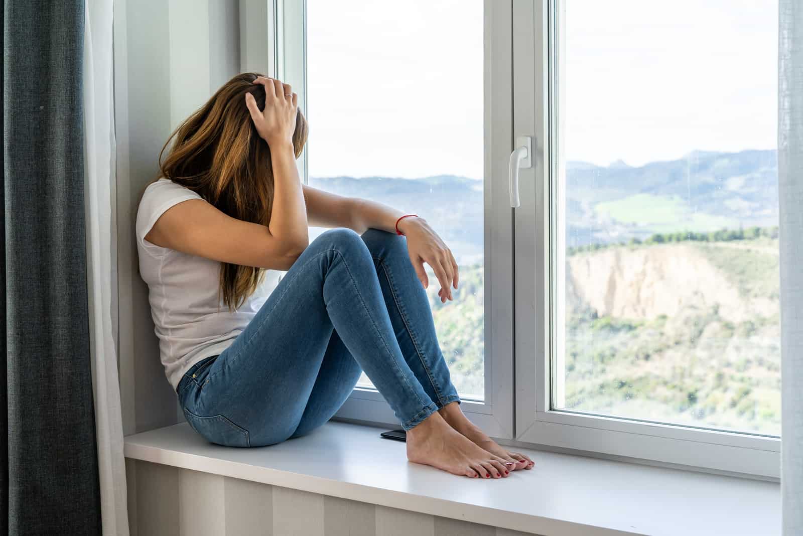 une jeune femme aux longs cheveux bruns est assise près de la fenêtre