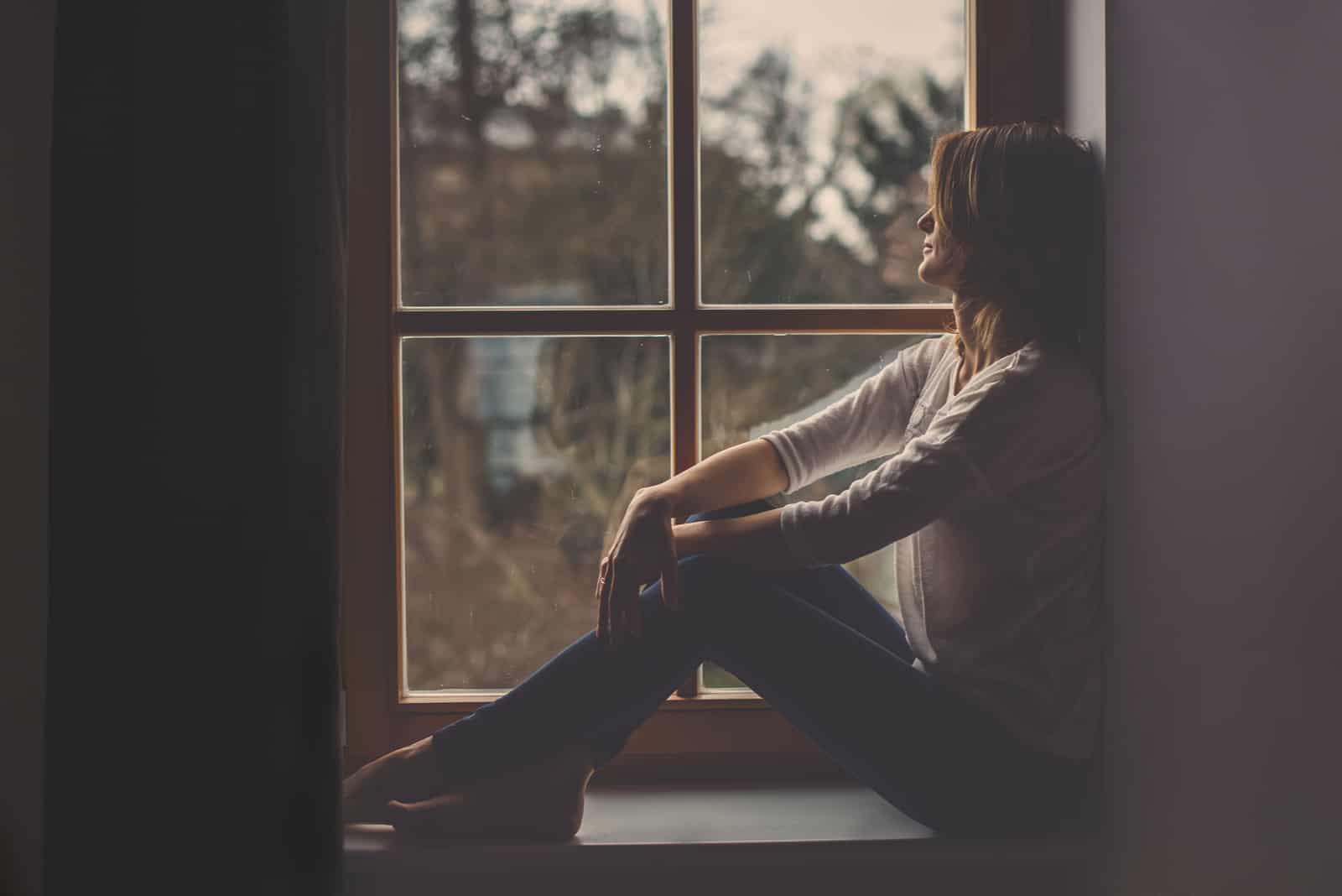 une jeune femme est assise pensivement près de la fenêtre et regarde