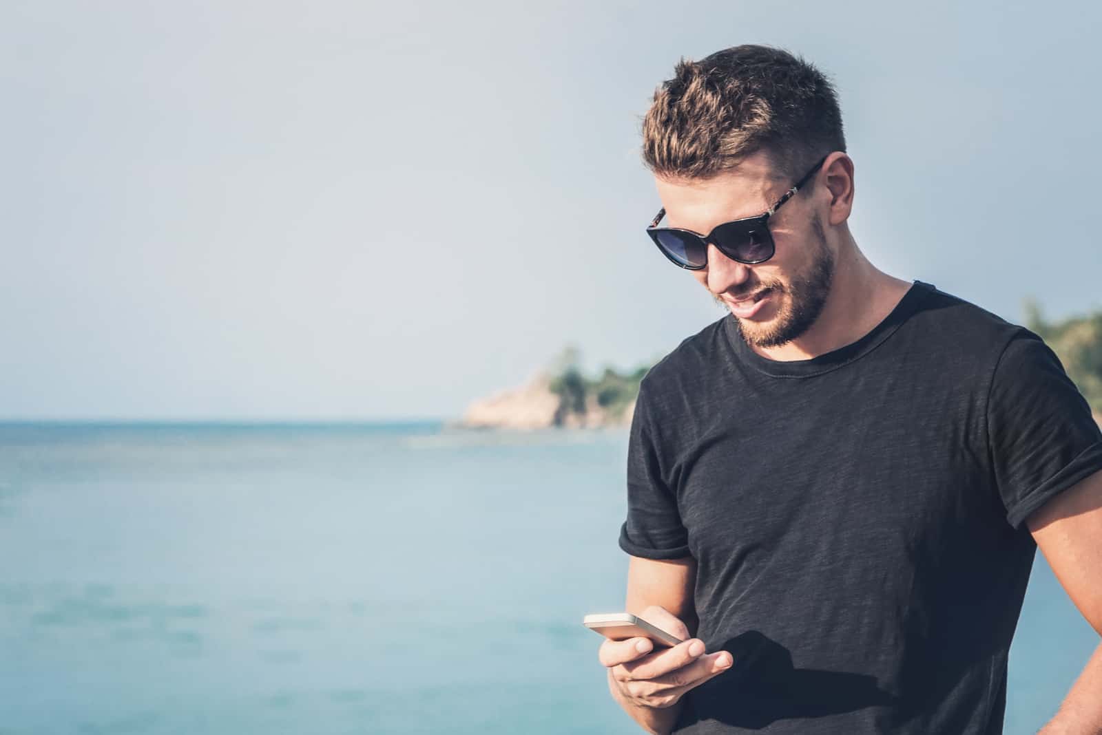 Bel homme à lunettes de soleil tenant un téléphone mobile