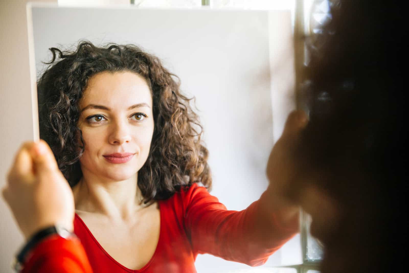 Femme aux cheveux bouclés, debout devant un grand miroir