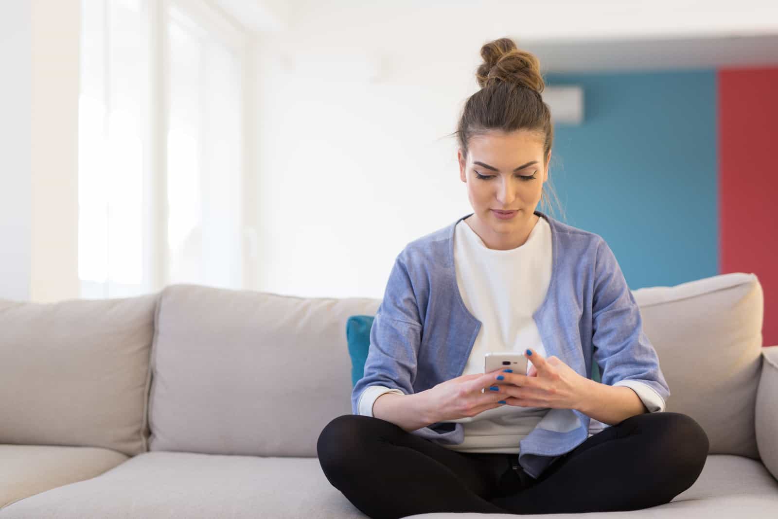 Femme utilisant un téléphone portable sur un canapé à la maison de luxe