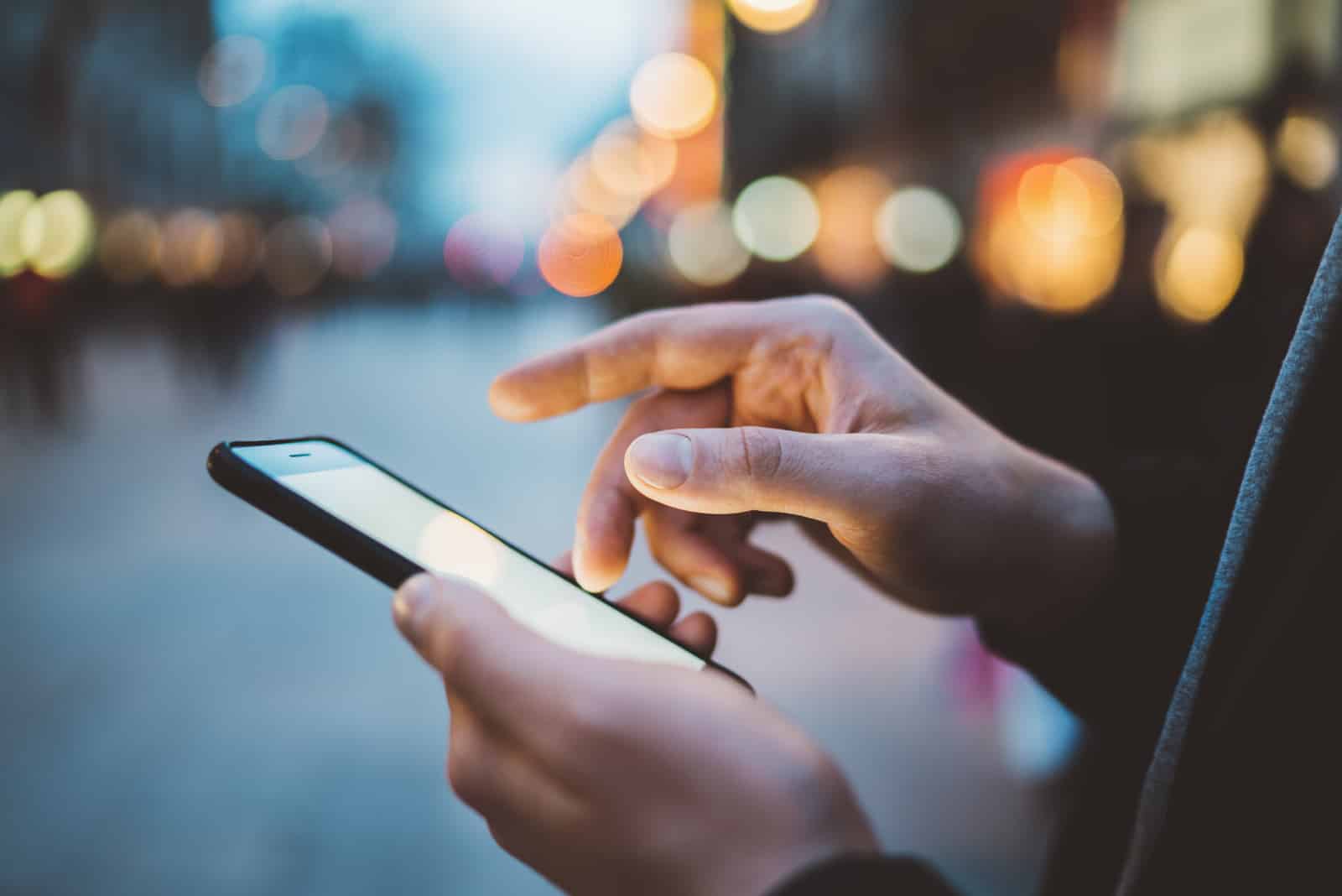 Mains mâles à l'aide de smartphone la nuit sur la rue commerçante de la ville