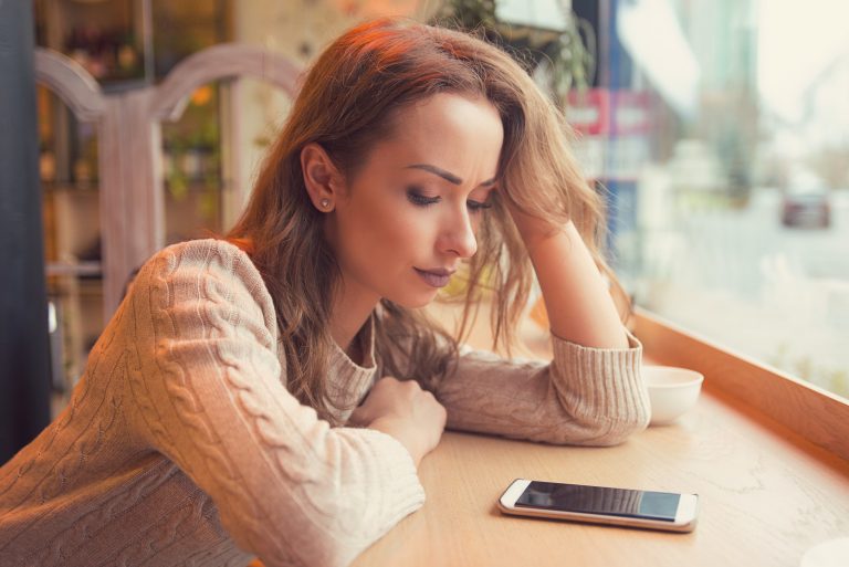 Une femme imaginaire assise dans un café à une table et regardant le téléphone