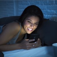 une femme souriante se trouve dans son lit et les touches du téléphone
