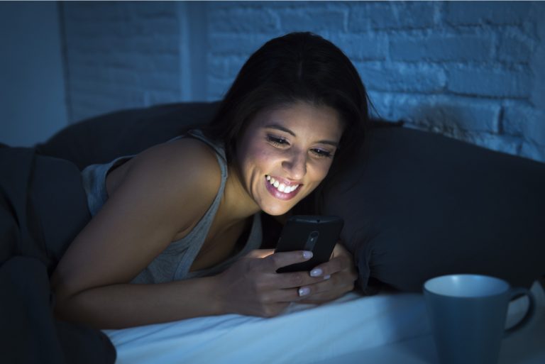 une femme souriante se trouve dans son lit et les touches du téléphone