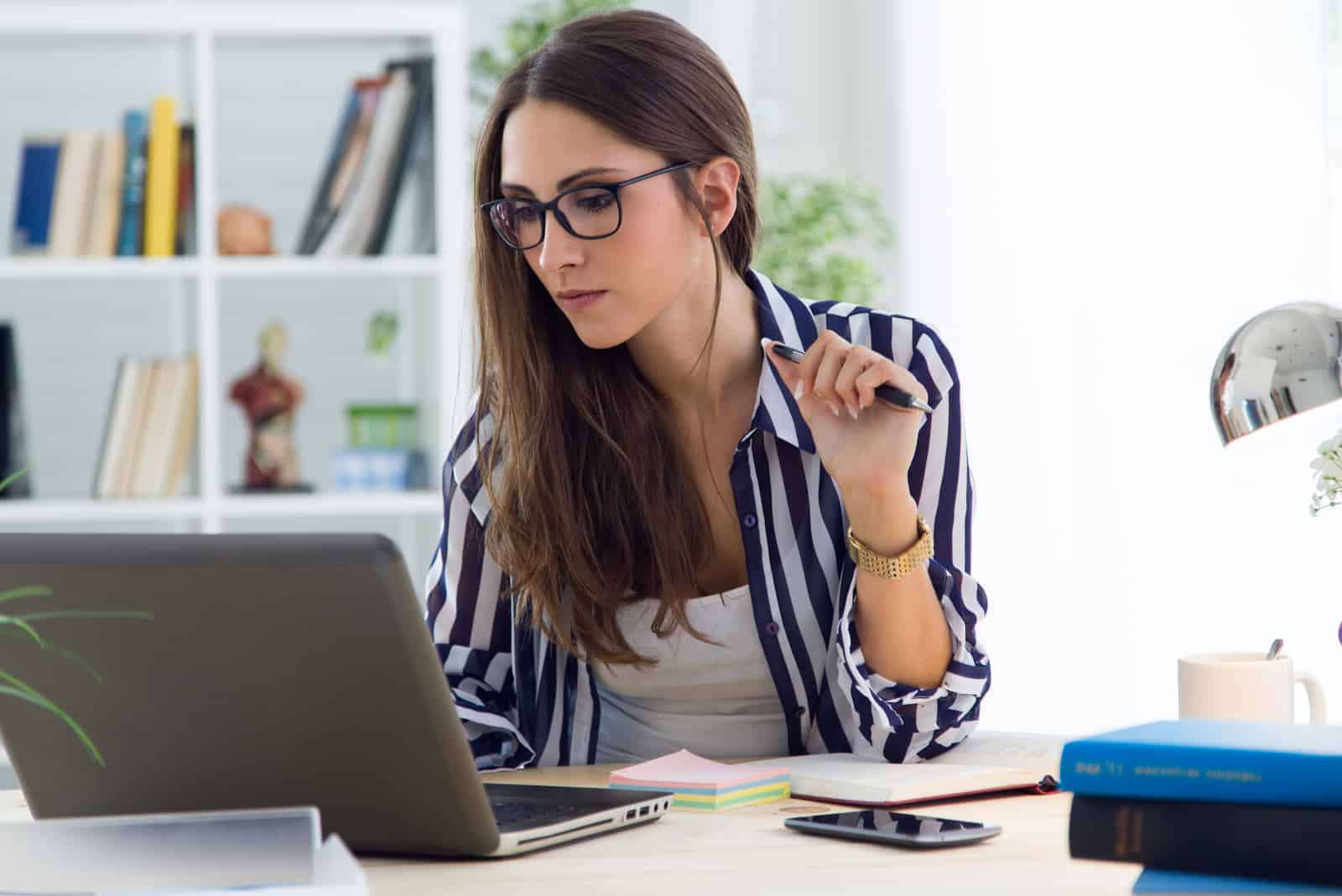 Une femme aux longs cheveux noirs avec des lunettes travaille derrière un ordinateur portable