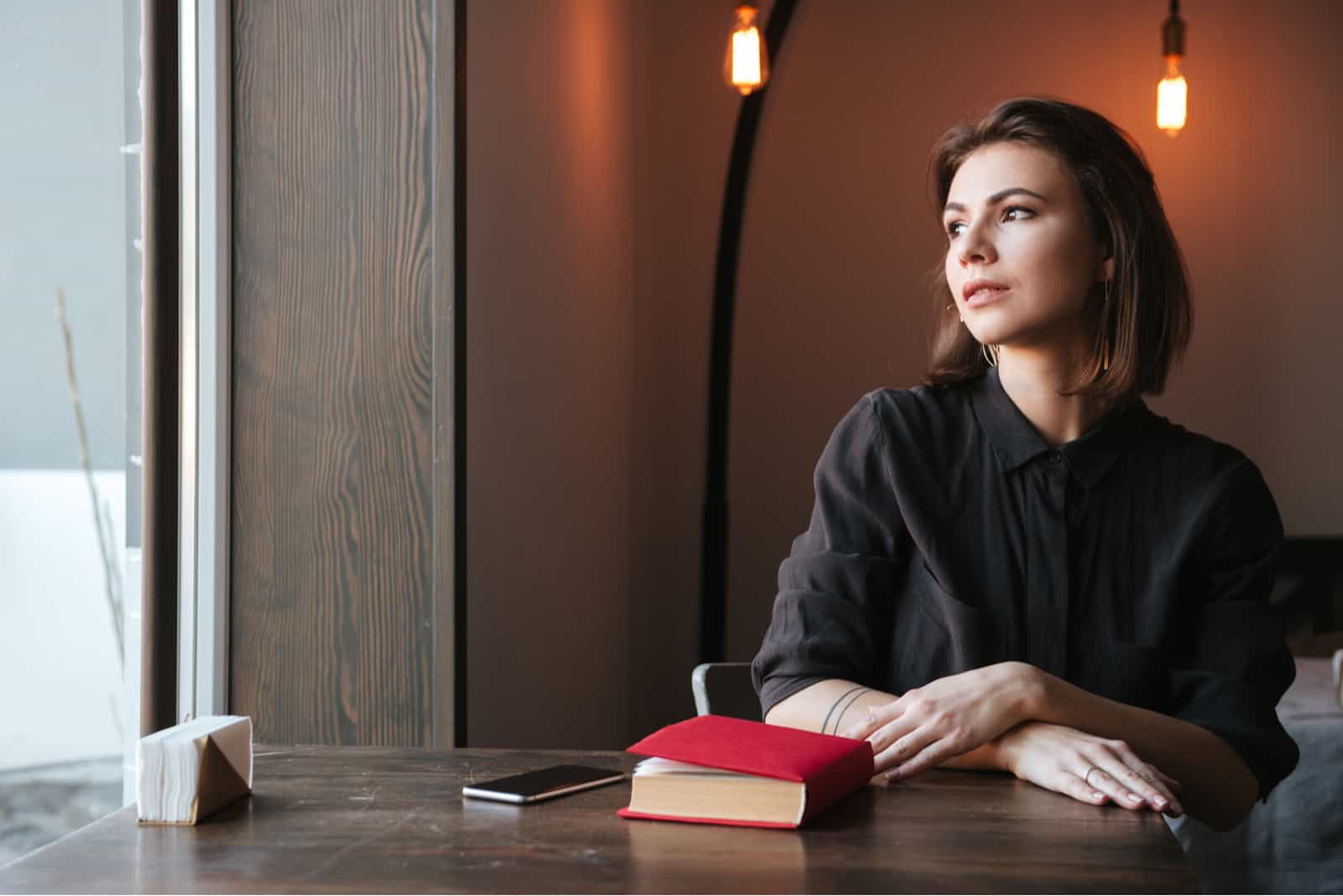 femme assise à la table près de livre et téléphone au café