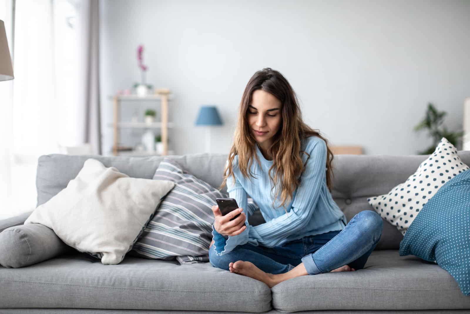 femme à l'aide de smartphone assis sur le canapé
