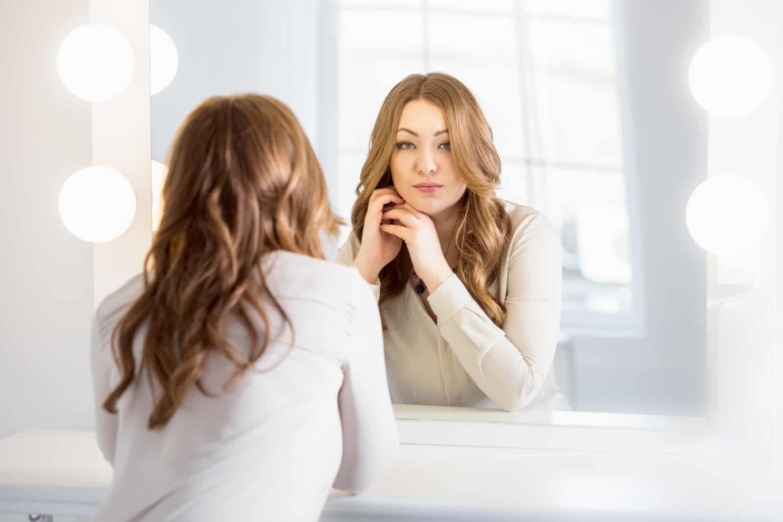 femme élégante aux cheveux bouclés regardant la réflexion dans le miroir