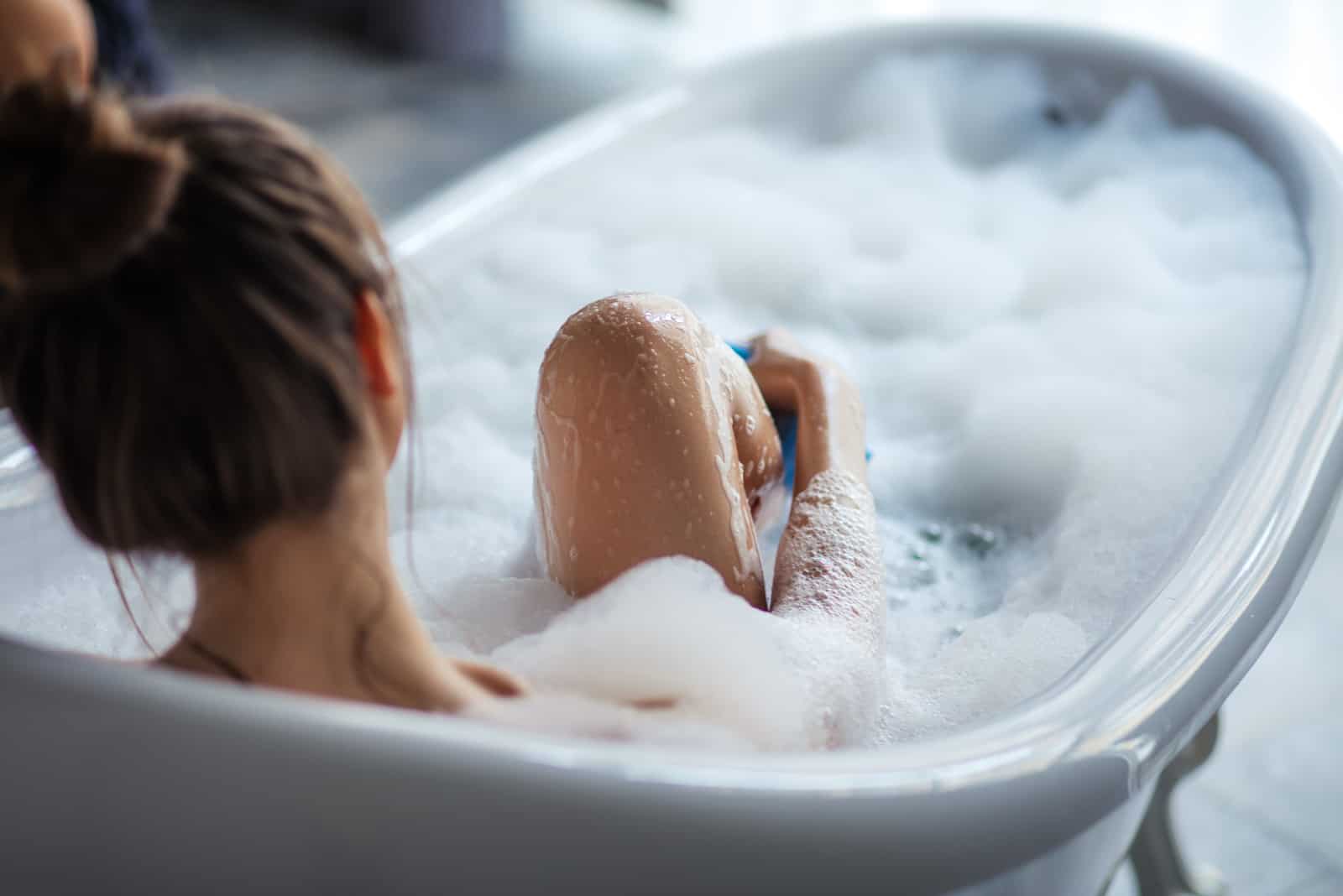 femme massant ses jambes avec une éponge dans la baignoire