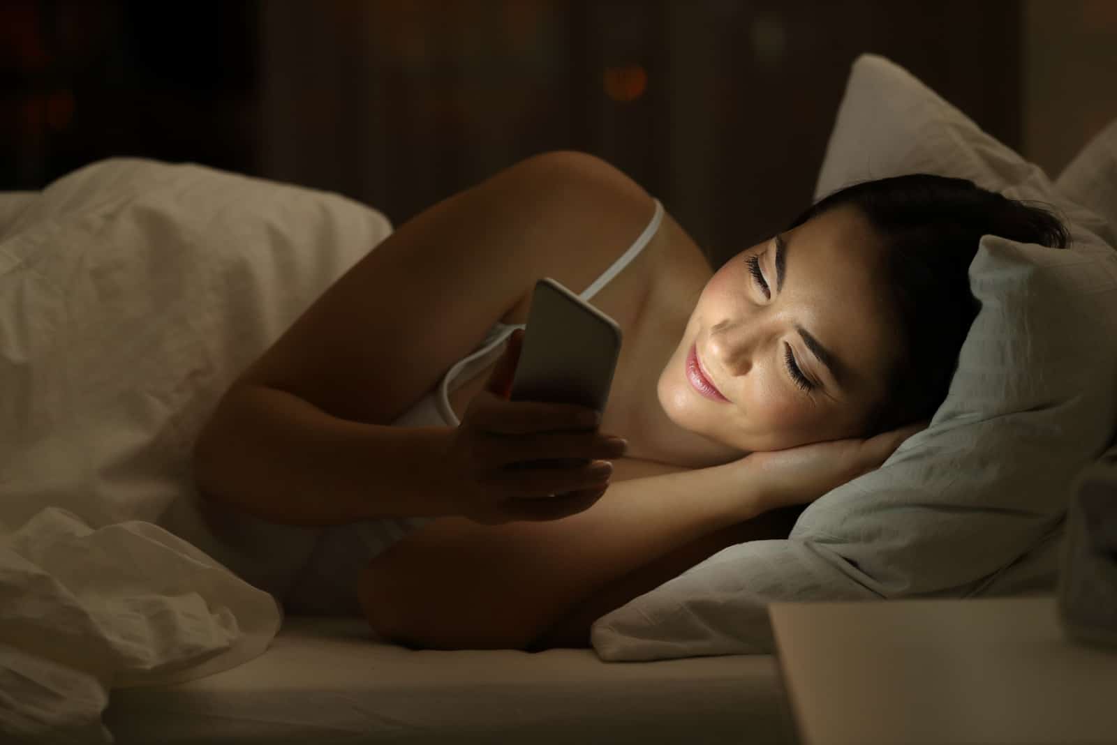 femme tenant téléphone allongé sur le lit dans la nuit