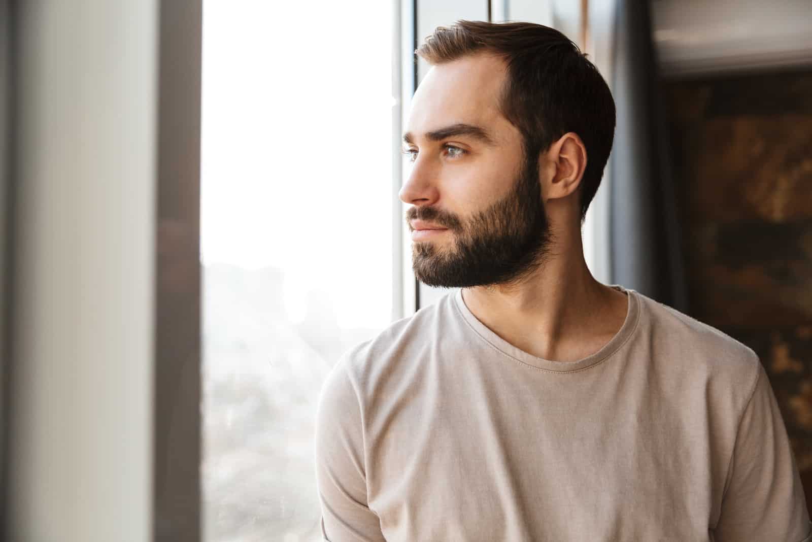 homme barbu debout à la fenêtre à la maison