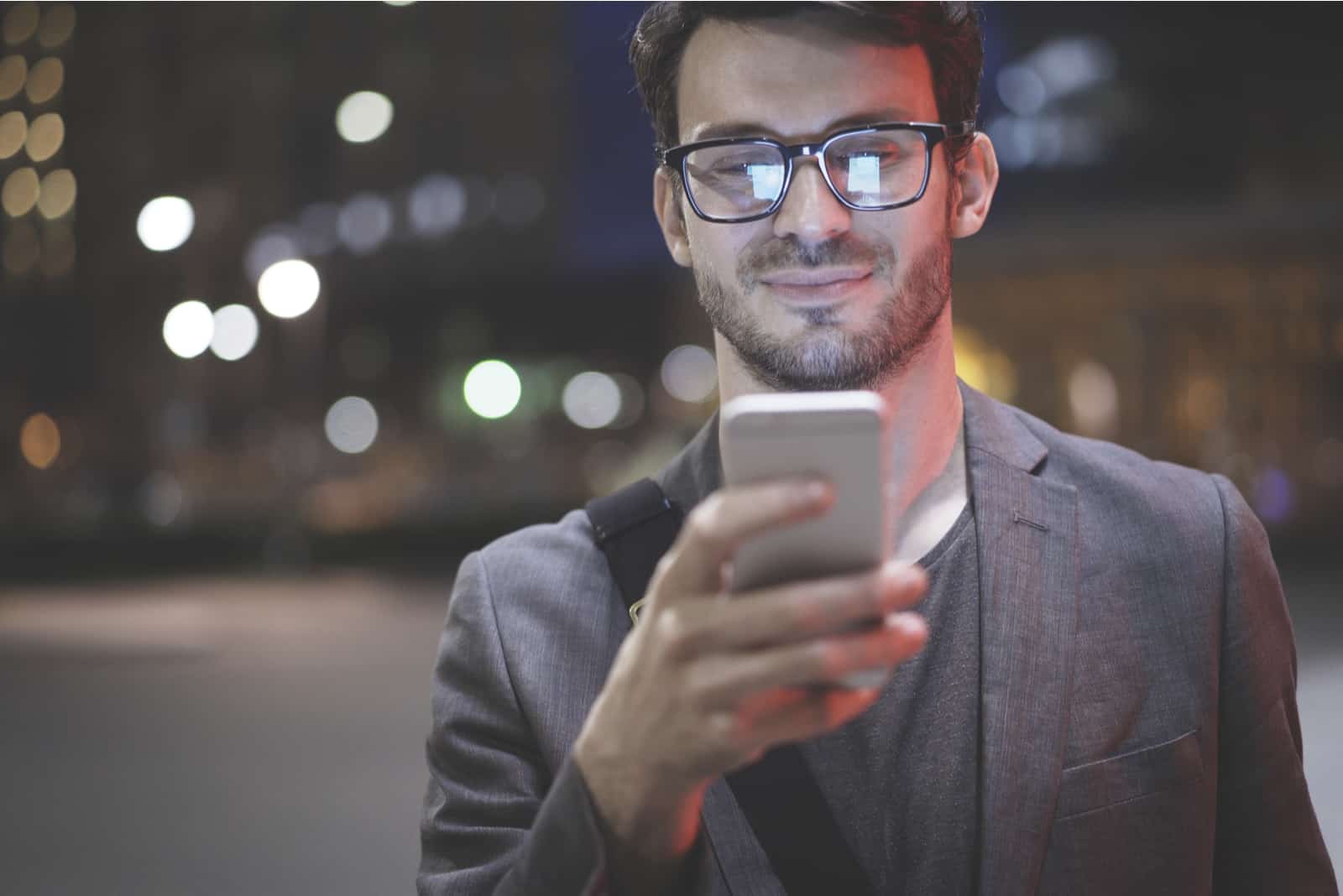 homme portant des lunettes tient des textos de défilement dans son téléphone portable
