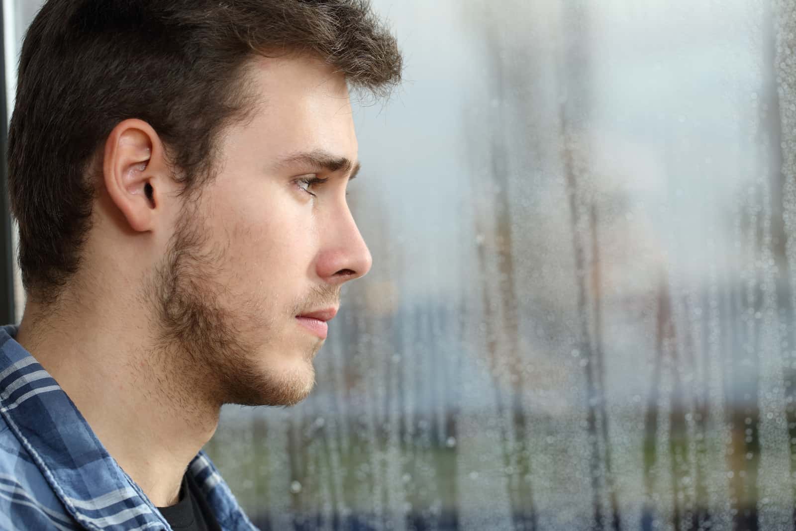 homme regardant par la fenêtre dans un triste jour de pluie