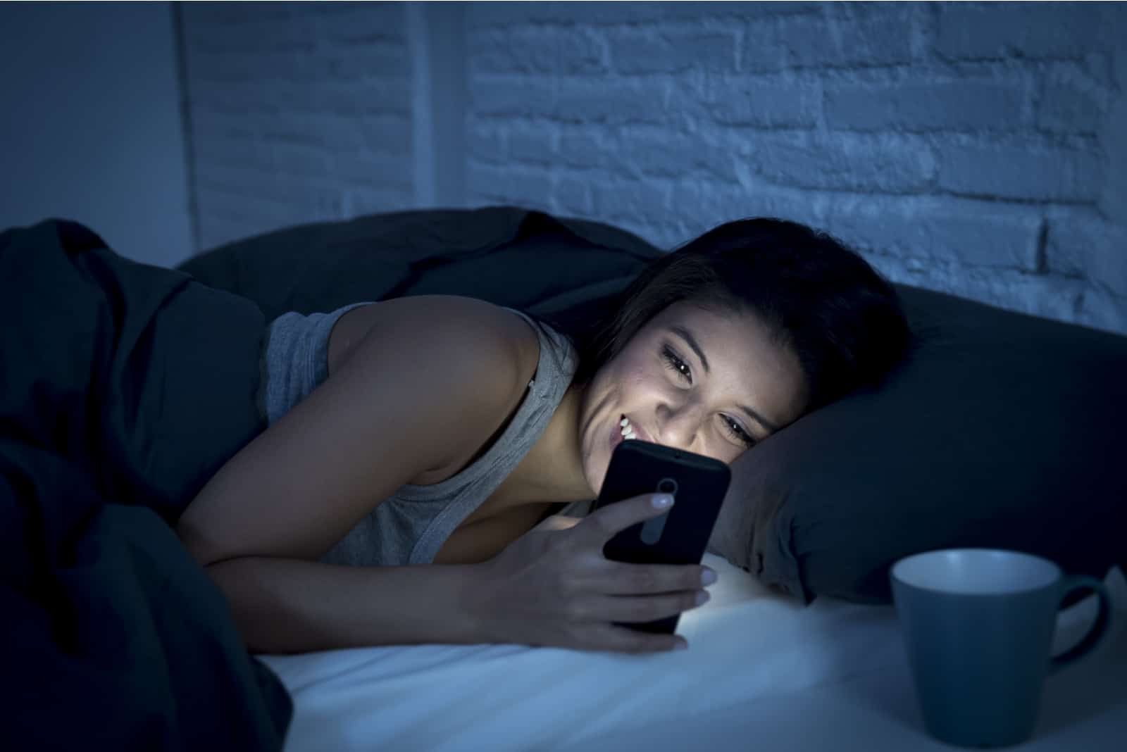 la femme est allongée dans son lit tenant un téléphone à la main