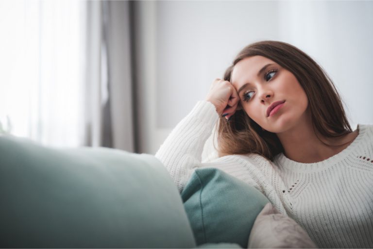 Femme triste en pull blanc assis sur un canapé