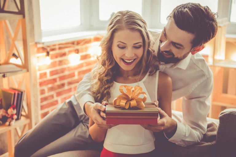 Beau jeune couple fête à la maison. Bel homme donne à sa petite amie une boîte-cadeau