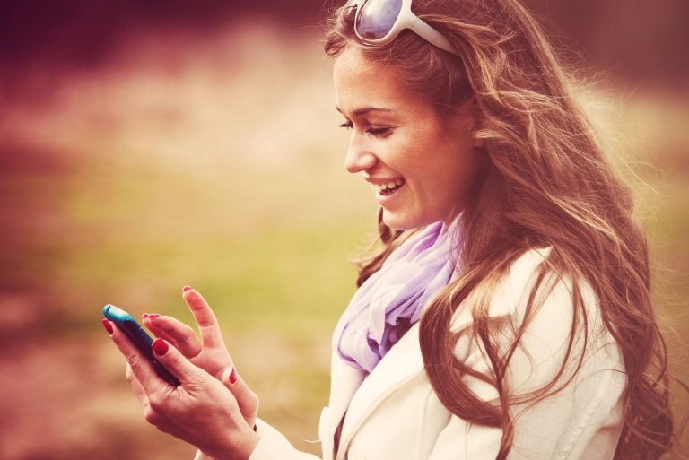 Femme souriante lisant un message sur un téléphone intelligent, prise de vue en extérieur, couleurs rétro.