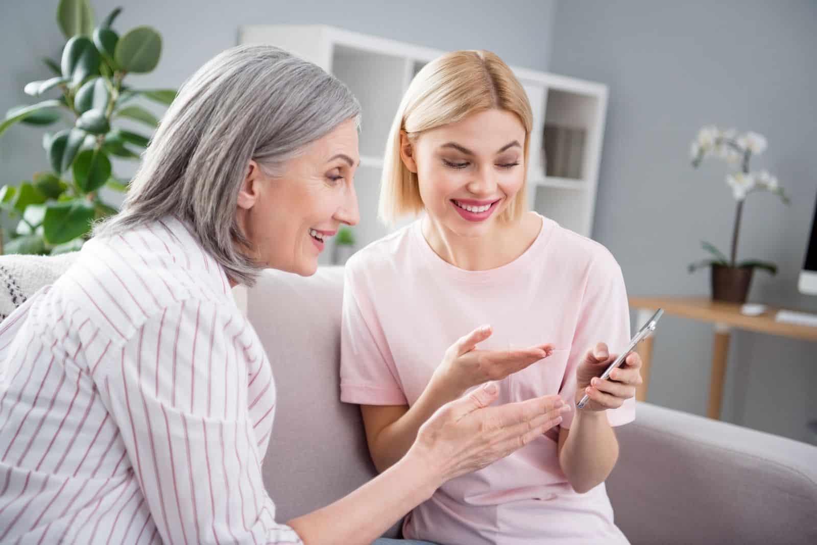 Photo de joyeux joyeux belle jeune femme et vieille dame regarder téléphone expliquer à l'intérieur à l'intérieur de la maison maison appartement