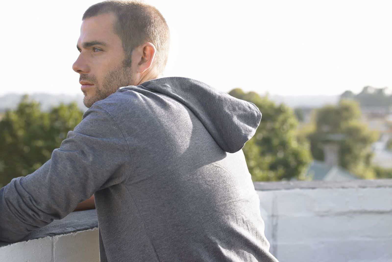 Vue latérale du jeune homme réfléchi appuyé sur le mur à l'écart