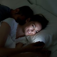 Une femme utilise un smartphone alors qu'elle est allongée à côté d'un homme au lit