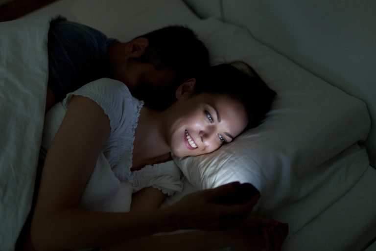 Une femme utilise un smartphone alors qu'elle est allongée à côté d'un homme au lit