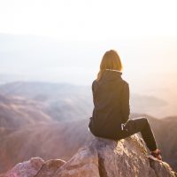 femme assise sur un rocher en regardant le coucher du soleil