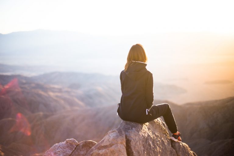 femme assise sur un rocher en regardant le coucher du soleil