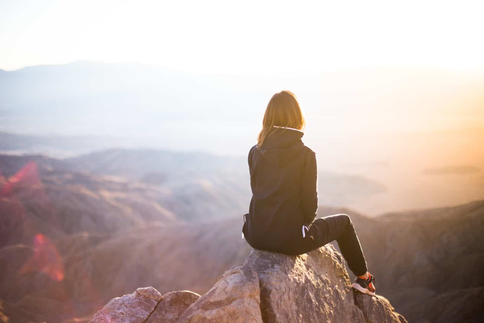 femme assise sur un rocher en regardant le coucher du soleil