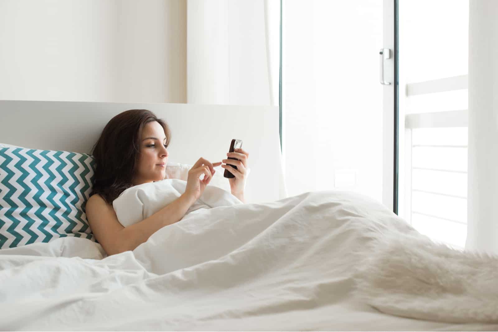Femme au lit, vérification des applications sociales avec smartphone