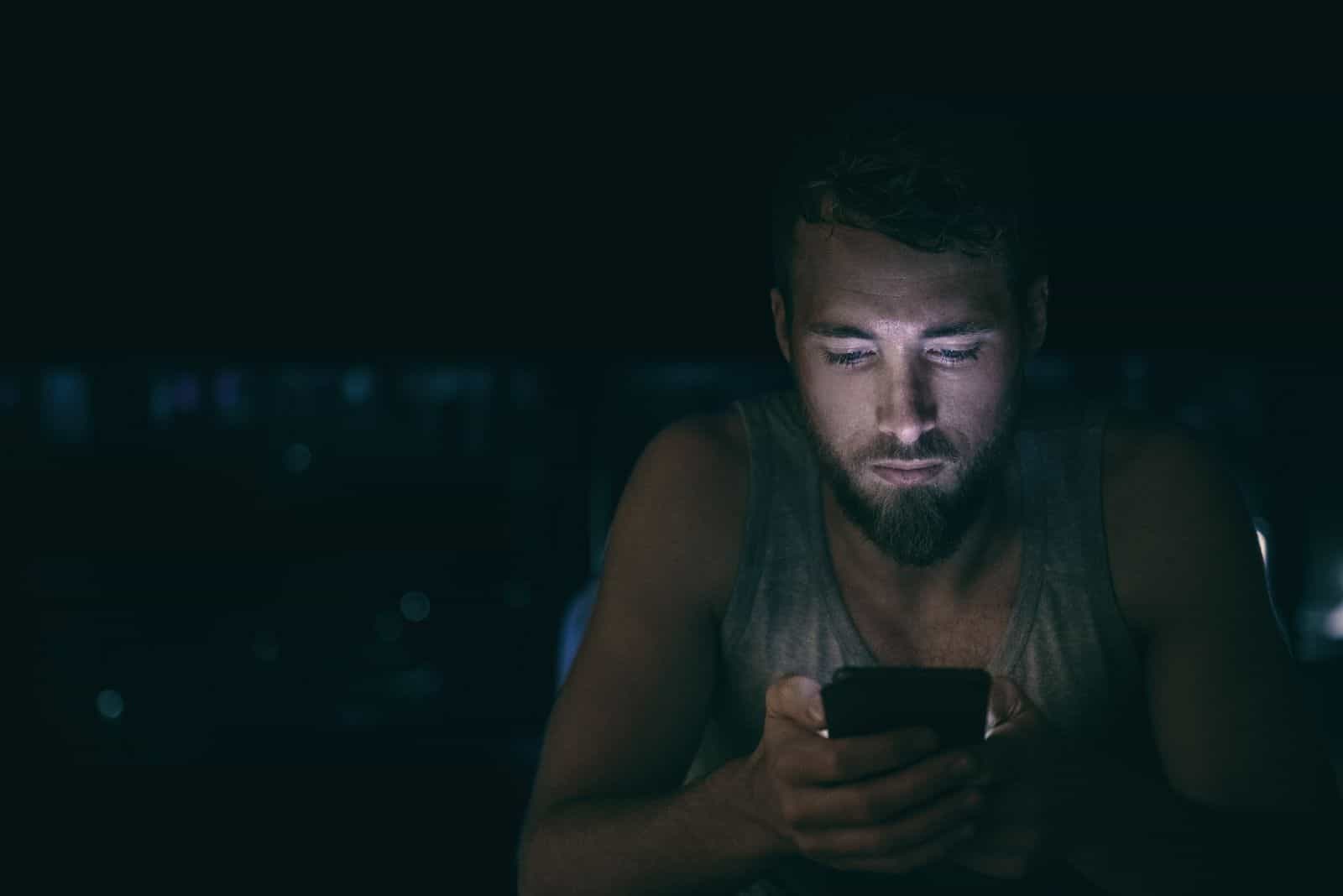 Homme de nuit noire regardant l'écran du téléphone mobile textos tard dans la nuit éveillé dans son lit