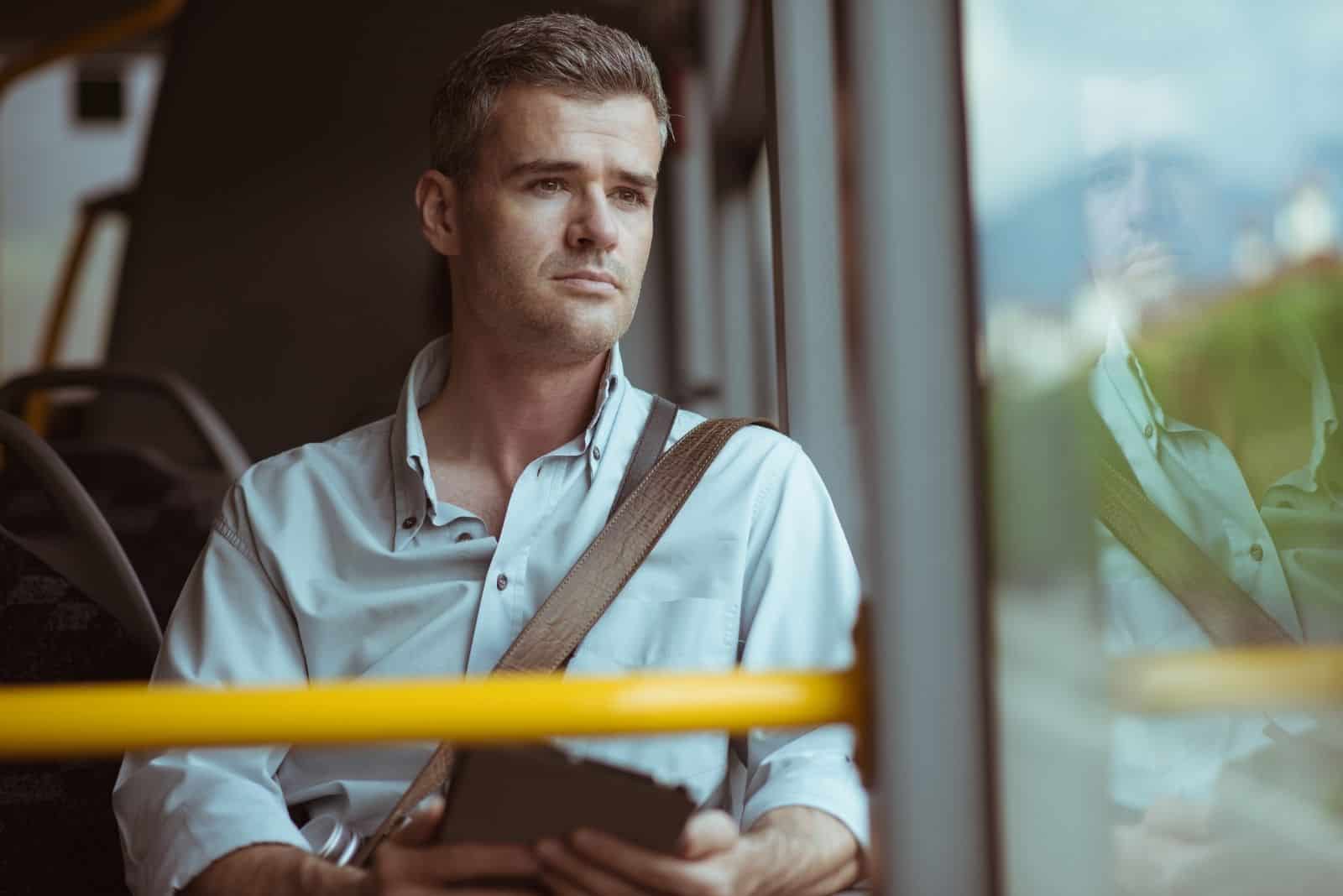 Homme pensif confiant assis sur le bus, il regarde à travers une fenêtre et à l'aide d'une tablette numérique