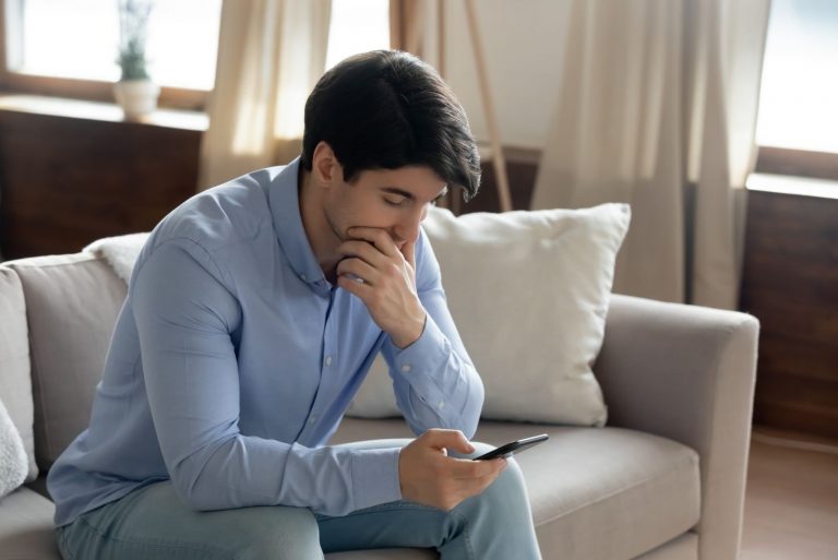 Gros plan homme sérieux réfléchi touchant le menton, regardant l'écran du smartphone, ayant un problème avec le téléphone ou la lecture de mauvaises nouvelles dans le message