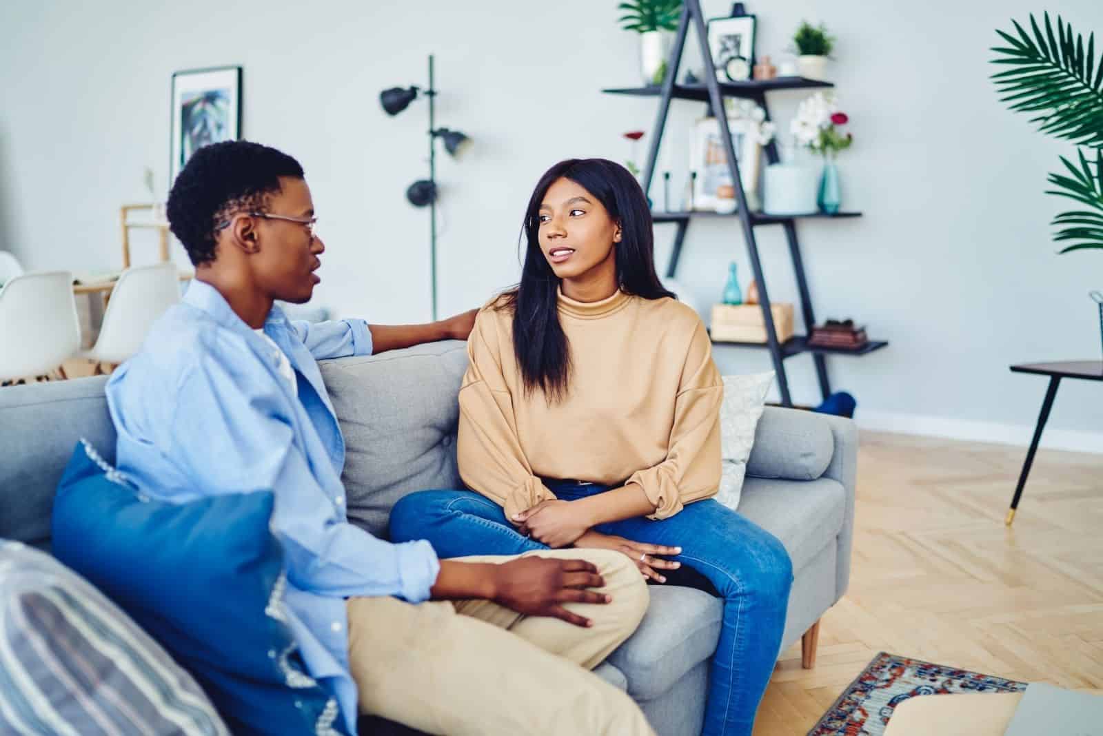 Jeune couple afro-américain amoureux parler les uns aux autres assis à un canapé confortable dans le salon ensemble