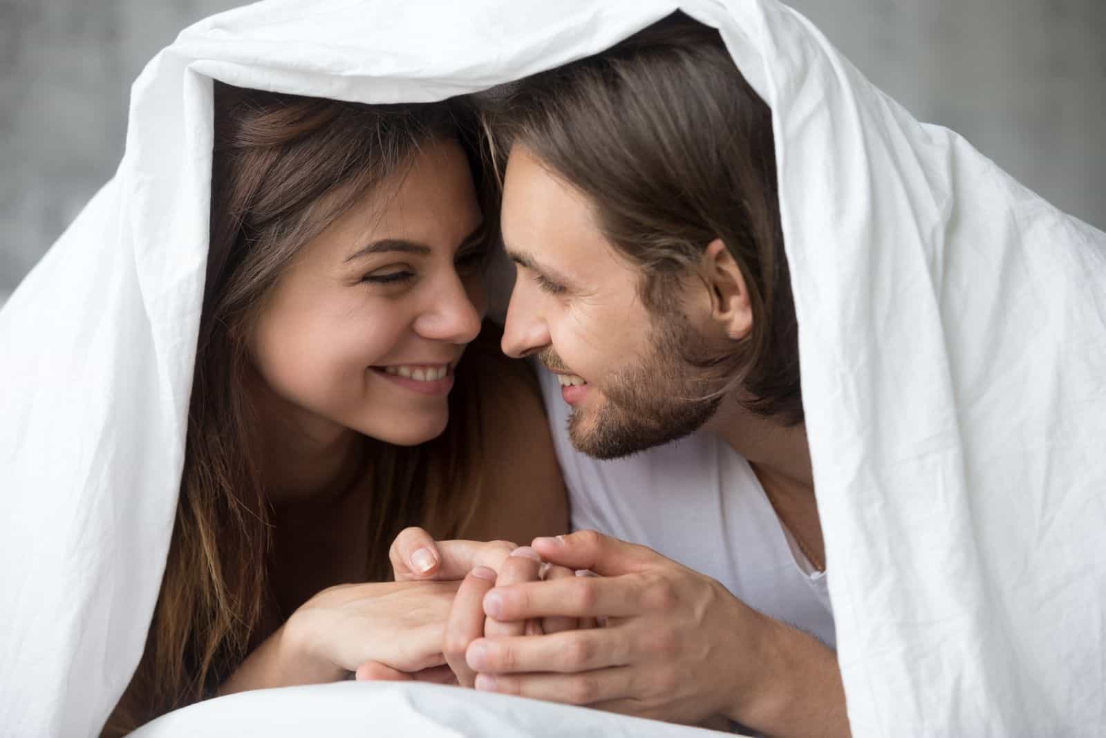 Jeune couple souriant s'amusant dans un lit recouvert d'une couverture chaude et douce