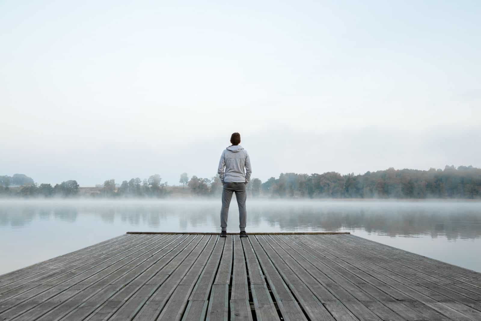 Jeune homme debout seul sur une passerelle en bois et regardant le lac.